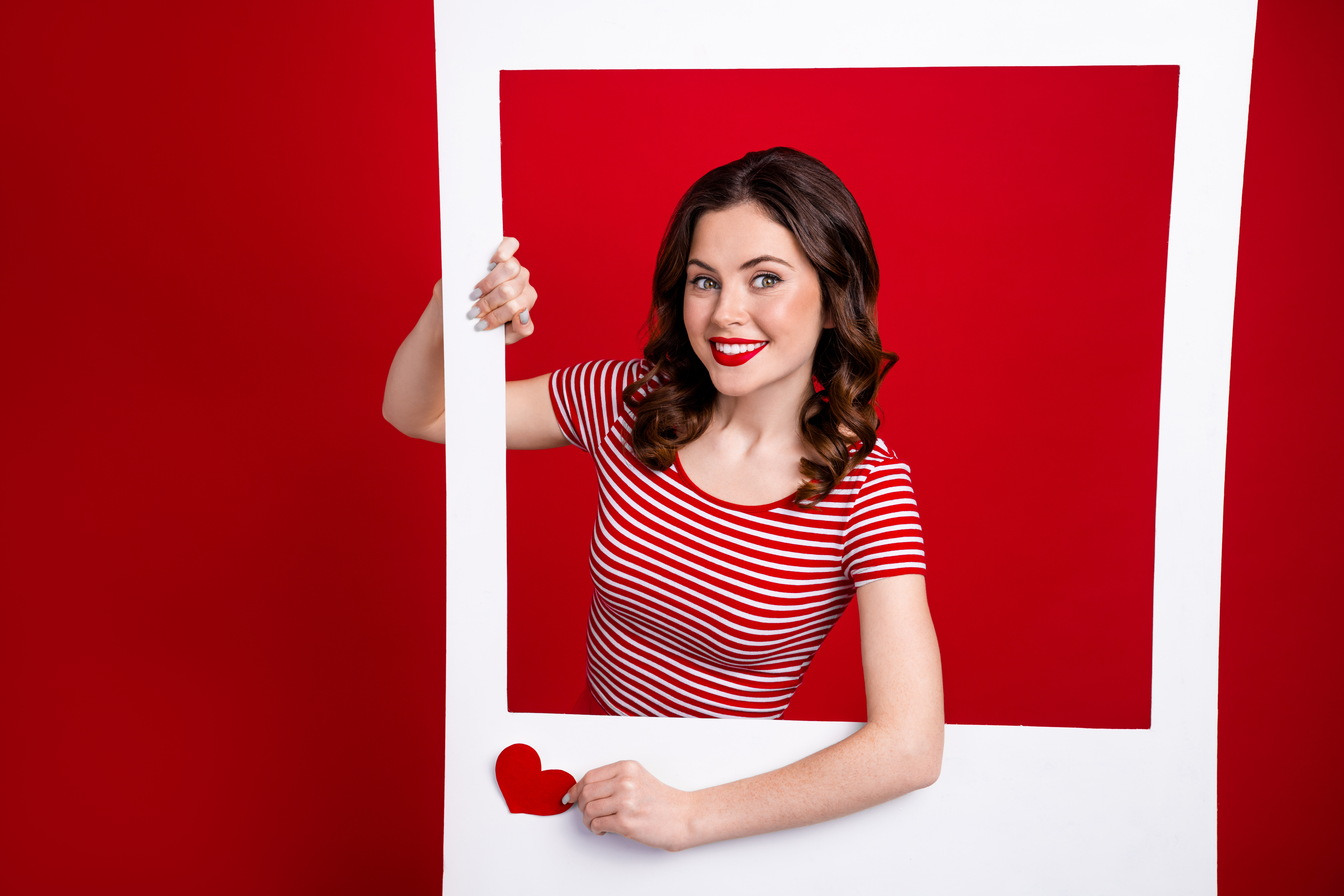 Blogueira adorável fotografando uma grande moldura de papel branco para likes no post do instagram vestindo uma blusa listrada em um fundo vermelho